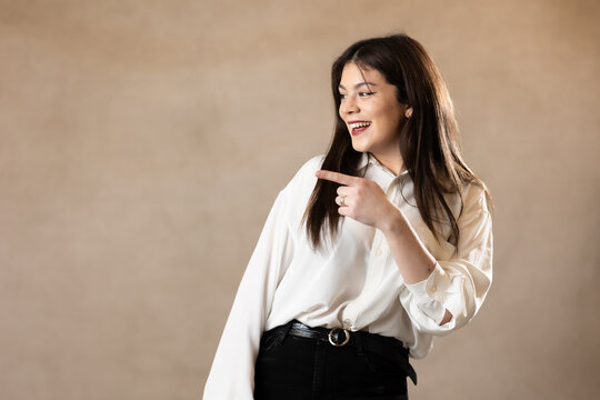 chica joven mujer morena con camisa blanca se&ntilde;alando a un lado y sonriendo