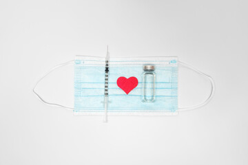 Injection syringe and corona virus vaccine on medical mask, with red heart.