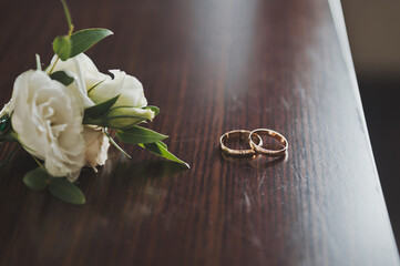 Wedding gold rings lie with white flowers on a brown table 2595.