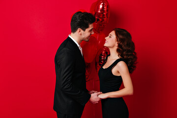 Happy couple holding hands isolated on red. Studio shot of man celebrating valentine's day with girlfriend.