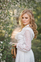 Fototapeta premium A girl in a white dress with lace and a straw hat in her hands is standing in the garden 2684.