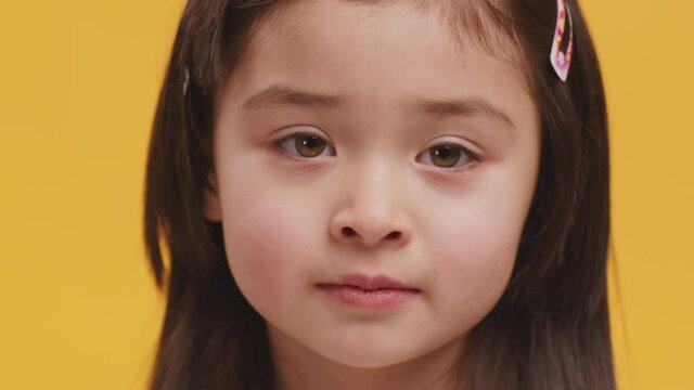 Shhh, it's secret. Close up of little girl putting finger on lips, showing silence gesture, orange studio background