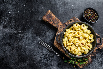 Italian tortellini pasta with cheese sauce in a pan. Black background. Top view. Copy space - obrazy, fototapety, plakaty
