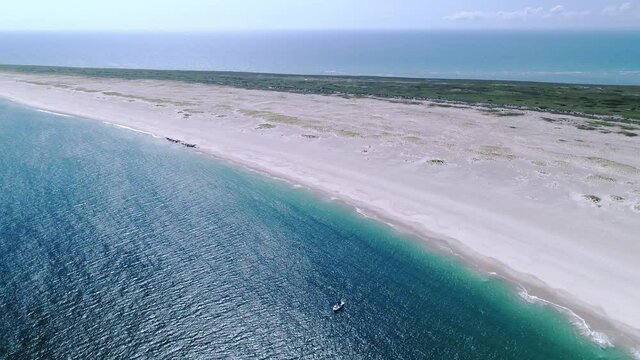 Drone flying around a boat in emerald water on the coast of a national wildlife preserve