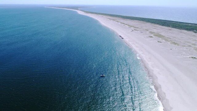 Drone flying forward toward a boat in emerald water on the coast of a national wildlife preserve