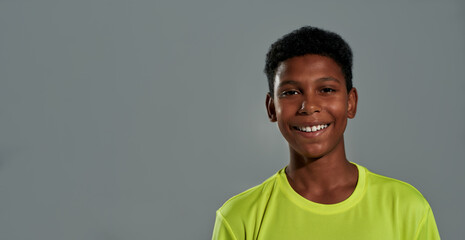 Portrait of a cheerful teenage african boy smiling at camera, posing isolated over grey background