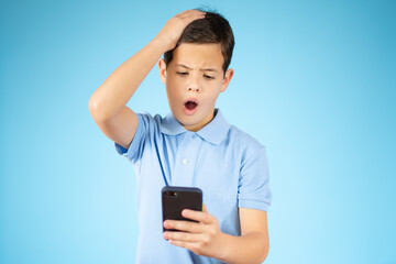 Fototapeta premium Cute ginger kid with mobile phone on blue studio background, using exciting mobile applications or chatting with friends, copy space.