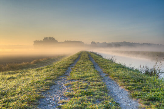 Autumn morning on the Schaalsee Canal. Fog has formed over the fields and drifts like a cloud over the dam on the canal. The sun bathes the landscape in its warm light.