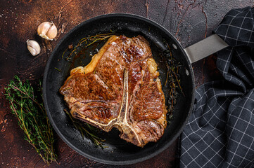 BBQ Grilled t-bone beef meat Steak with herbs on a plate. Dark background. Top view