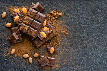 Broken pieces of almond chocolate and cocoa powder on a wooden background