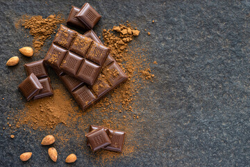 Broken pieces of almond chocolate and cocoa powder on a wooden background