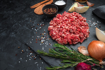 Juicy, fresh minced meat with spices on a flat plate on a black background. Side view, horizontal.