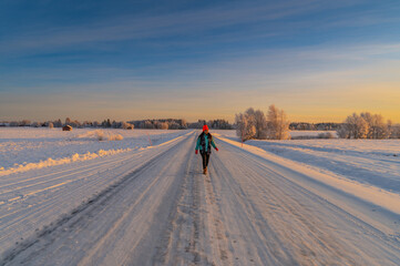 A beautiful solo traveller woman wearing colourful cloth walking on the empty road with snow covered scenic landscape view and sun light