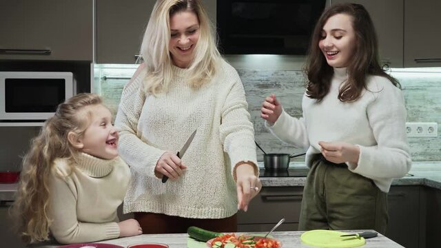 Young mother and two her daughters cooks salad at kitchen. Mother salt salad. Salt bae