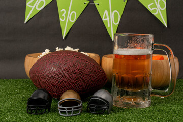 American football party. American football ball, beer, little helmets, snacks and banner on green...