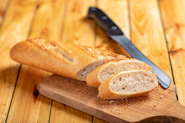 Tasty and fresh baguette cut into pieces. Bread and a chopping knife in the home kitchen.