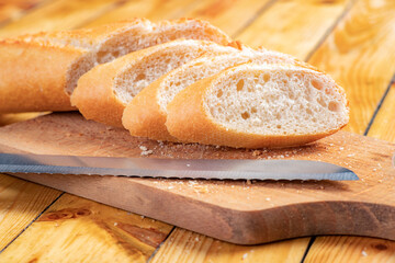 Tasty and fresh baguette cut into pieces. Bread and a chopping knife in the home kitchen.