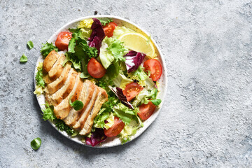 Mix salad with tomatoes and chicken fillet in a plate on a concrete background.
