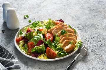 Mix salad with tomatoes and chicken fillet in a plate on a concrete background.