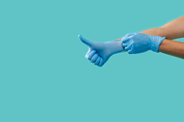 Doctor's hands puts on medical gloves stretching the rubber and showing a thumb up on a blue...