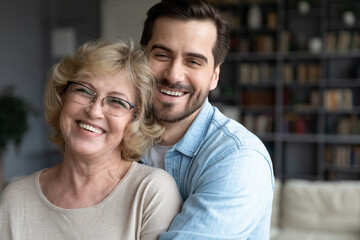 Head shot close up portrait happy young european appearance man cuddling elderly retired mother in...