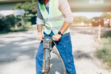 Young male road construction worker at his job. Bright sunny day. Strong light.