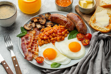 Full English breakfast on a plate with fried eggs, sausages, bacon, beans, toasts and coffee on light stone background. Top view