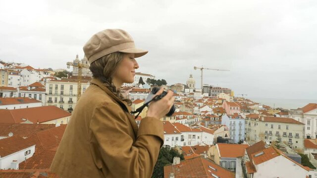 A young millennial tourist takes pictures of the sights in historic center of Lisbon against the backdrop of ancient temples on the tourist viewing platform