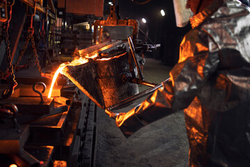 Casting and foundry. Worker in protection suit pouring liquid steel into molds. Metallurgy and...