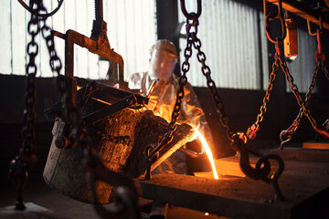 Worker in foundry pouring hot metal into mold. Molten iron casting production and metallurgy.