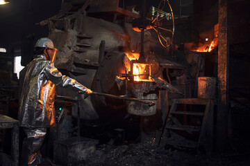 Foundry worker pouring hot steel into bucket for metal casting. Iron production and melting.