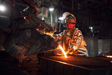 Foundry hardworking people pouring hot liquid iron from bucket into molds. Iron ore production and...