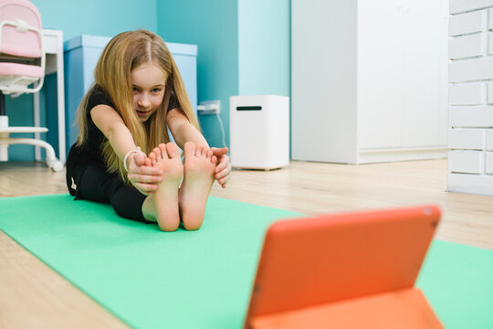 Girl make home stretching exercise with tablet