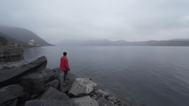 Hiker In Red Looking Out Over Misty Fjord