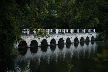 Fototapeta premium old historical stone bridge, romantic view on the dam and its reflection on the surface of the pond and broadleaved forest, Rokytka in Dolni Pocernice, Prague