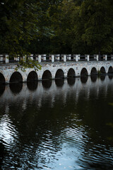 Fototapeta premium old historical stone bridge, romantic view on the dam and its reflection on the surface of the pond and broadleaved forest, Rokytka in Dolni Pocernice, Prague