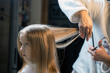 Fototapeta premium hair cutting at home, mom cuts daughter's hair in the kitchen