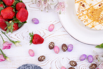 Festive Easter cake topped with white cream and nuts, strawberries and chocolate eggs in a multi-colored wrapper and spring flowers