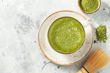 Matcha green tea latte in a cup with cream on a light concrete background. Top view with copy space