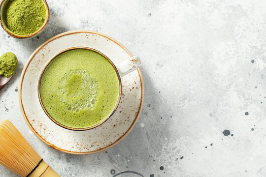 Matcha green tea latte in a cup with cream on a light concrete background. Top view with copy space