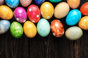 Different easter eggs with straw on wooden plate on green table