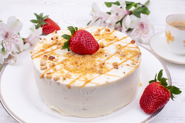 Festive Easter cake topped with white cream and nuts, strawberries and chocolate eggs in a multi-colored wrapper and spring flowers