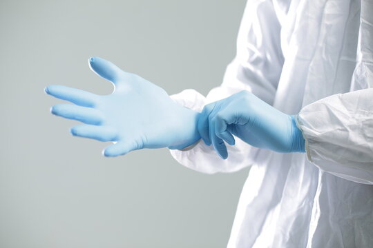 Doctor in a protective suit puts on blue rubber gloves