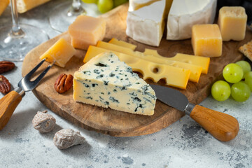 Tasting cheese dish on a wooden plate. Food for wine and romantic date, cheese delicatessen on a light concrete background