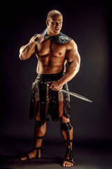 Fototapeta na wymiar Severe barbarian in leather costume with two swords. Portrait of balded muscular gladiator. Studio shot. Black background.