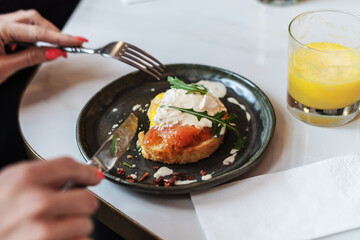 Woman hands holding fork and knife and having breakfast. Smoked salmon sandwich with cream cheese on plate close-up, glass of orange juice, napkin. Selective Focus