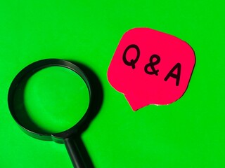 Q and A concept.Top view red bubble speech written Q and A with magnifying glass isolated on green background.