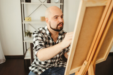 Naklejka na ściany i meble Art, creativity, professional occupation. Artist working in home studio. Man painting with watercolor at easel. Creative leisure and remote work concept