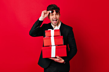 Well-dressed white man holding valentine presents. Studio shot of laughing guy isolated on red.