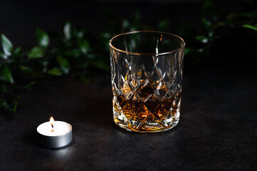 Close-up of an antique glass filled with whiskey or bourbon. The tumbler stands on a stone background, which creates a rustic scene (food photography)

